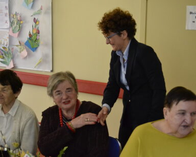 Zbliżenie. Pani prezydentka Sopotu składa życzenia siedzącym przy stole seniorkom.