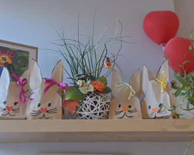 Półka. Na niej wielkanocne papierowe króliczki, kwiaty w doniczkach, balony serca i obraz.