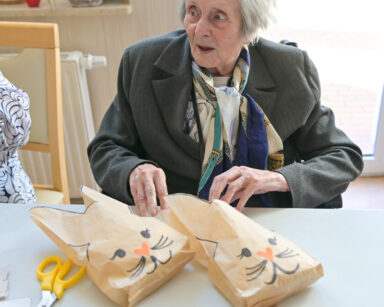 Zbliżenie. Seniorka przy stole siedzi i trzyma ręce na papierowych wielkanocnych króliczkach.