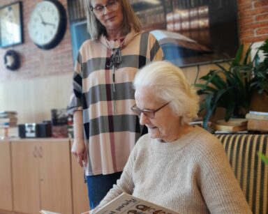 Zbliżenie. Seniorka siedzi na fotelu i trzyma w ręku książkę pt. 