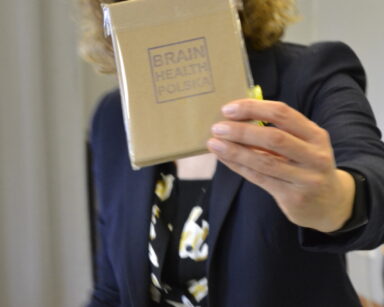 Zbliżenie. kobieta w granatowej marynarce wyciąga przed siebie książeczkę z napisem Brain Health Polska.