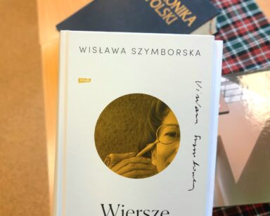 Zbliżenie. Na stole książka ze złotymi literami. Kronika Polski. W ręku książka Wisława Szymborska 