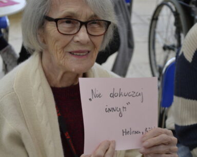 Zbliżenie. Seniorka trzyma w ręku kartkę z napisem