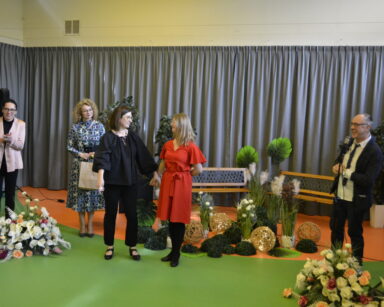Scena. Udekorowana roślinami, światełkami, ławki w tle. Na scenie cztery kobiety i mężczyzna przy mikrofonie.