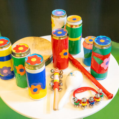 Zbliżenie. Na stoliku kolorowe puszki z nalepionymi kolorowymi kwiatami, flet, shaker perkusyjny i tamburiny.