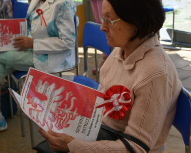 Zbliżenie. Dwie seniorki siedzą na krzesłach w dłoniach mają rozłożone teksty polskich piosenek patriotycznych.