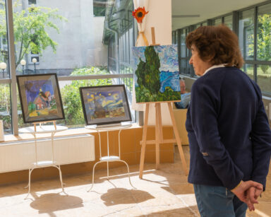 Sala. Na sztalugach postawione są trzy obrazy z krajobrazem , inspirowane Van Goghiem. Przed pracami stoi seniorka.