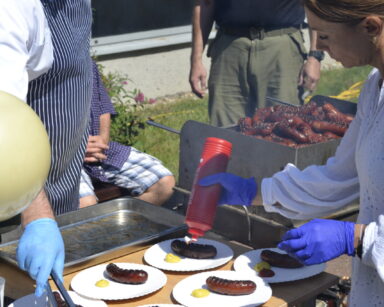 Zbliżenie. Grill. Kucharz rozkłada na talerze kiełbasy z grilla. Obok kobieta polew na talerze keczup i musztardę.