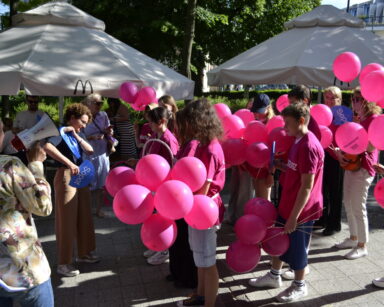 Miasto, promenada, drzewa, parasole. Kobieta z megafonem, obok Prezydentka Sopotu, grupa wolontariuszy z balonami.