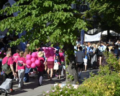 Miasto, promenada, drzewa, parasole. Maszeruje grupa ludzi w różowych koszulkach oraz sopocki klub lekkoatletyczny.