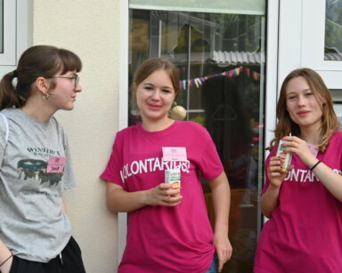 Zbliżenie. Trzy wolontariuszki, dwie w różowych koszulkach, jedna w szarej. Dwie dziewczyny trzymają w dłoni soczki.