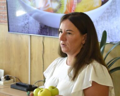 Zbliżenie. Kobieta w białej sukience trzyma w ręku zielone jabłko. W tle na monitorze zdjęcie sałatki owocowej.