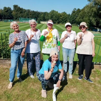 Stadion, grupa sześciu seniorek pozuje do zdjęcia. Seniorki trzymają w ręku medale. W tle boisko do piłki nożnej.