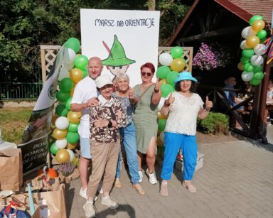 Zbliżenie. Cztery kobiety i mężczyzna pozują do zdjęcia. W tle kolorowe balony. Plakat z napisem 