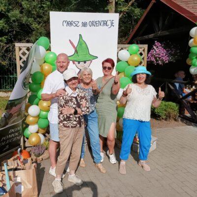 Zbliżenie. Cztery kobiety i mężczyzna pozują do zdjęcia. W tle kolorowe balony. Plakat z napisem "Marsz na orientację".