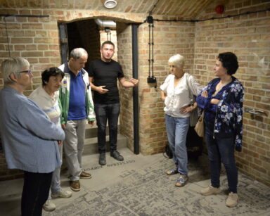 Sala. Na podłodze mapa Sopotu. Przed mapą w języku niemieckim napis uzdrowisko Sopot. W sali grupa seniorów i przewodnik.