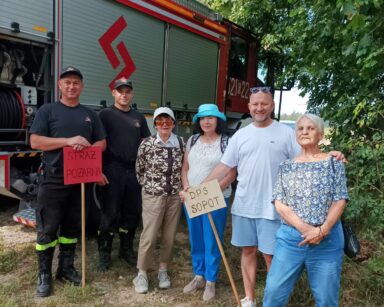 Zbliżenie. Dwóch strażaków, trzy seniorki i mężczyzna z DPS SOPOT, pozują do zdjęcia przy wozie strażackim.