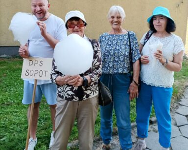 Zbliżenie. Cztery osoby pozują do zdjęcia. Mężczyzna i seniorka jedzą watę cukrową, dwie seniorki obok uśmiechają się.