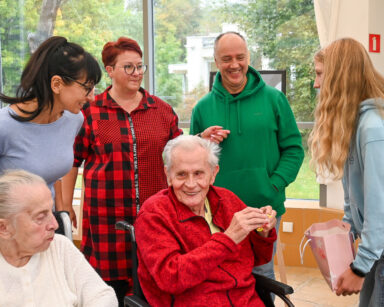 Zbliżenie. Trzech dorosłych ludzi, jedna nastolatka i dwóch seniorów na wózku pozują do wspólnego zdjęcia.