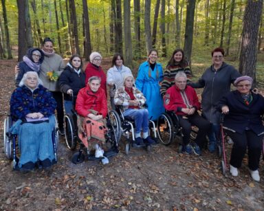 Las. Grupa seniorów na wózkach, wolontariuszy i opiekunów z DPS pozują do grupowego zdjęcia.