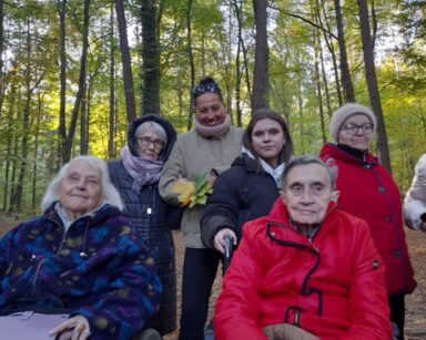 Zbliżenie. Sześć osób pozuje do zdjęcia. Dwie seniorki na wózku, cztery osoby stoją. Wszyscy ubrani w ciepłe kurtki.