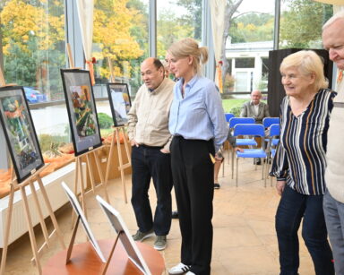 Sala. Wystawa obrazów na sztalugach. Przy obrazach stoi grupa ludzi.