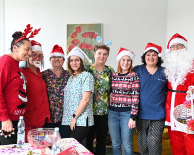 Zbliżenie. Siedem kobiet w przebraniach świątecznych i Mikołaj z koszem słodyczy pozują do grupowego zdjęcia.