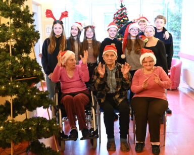 Zbliżenie. Choinka. Czterech seniorów, grupa młodzieży i trzy opiekunki DPS pozują do grupowego zdjęcia.