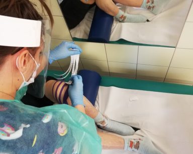 Fizjoterapeutka naklejająca taśmy kinezjologiczne na kalano seniorki