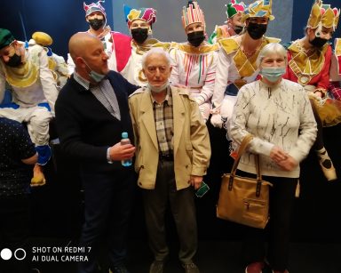 Sala teatru. Kierownik Arkadiusz Wanat i uczestnicy Dziennego Domu pozują do zdjęć z aktorami w kolorowych kostiumach.