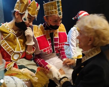Sala teatru. Seniorka rozmawia z dwoma aktorkami w kolorowych kostiumach.