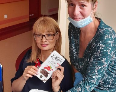Dyrektorka Agnieszka Cysewska trzyma czekoladę. Obok kierowniczka Ewa Siłakiewicz-Witt, trzyma tackę z kawałkami czekolady.