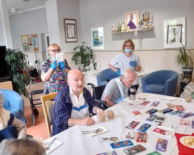Seniorzy przy stole. Na stole czekolady, kawa, papierowe talerzyki. Z tyłu opiekunki Katarzyna Weier i Małgorzata Kuświk.