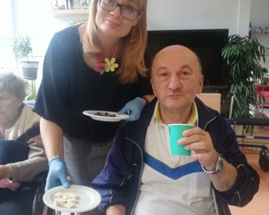 Dyrektorka Agnieszka Cysewska. W dłoniach trzyma talerzyki z czekoladą. Przy stole seniorzy.