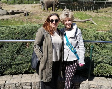 Pogodny dzień. Gdańskie ZOO. Terapeutka Gosia Jancelewicz i seniorka stoją uśmiechnięte. Na wybiegu słoń.