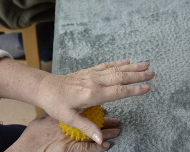 Zbliżenie na ręce starszej osoby. Masuje sobie dłoń piłeczką.