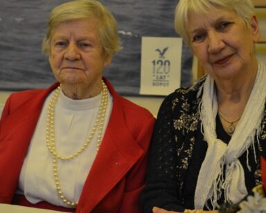 Sala. Przy stole siedzą dwie odświętnie ubrane seniorki. Na blacie talerzyk z makowcem.