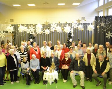 Sala. Zimowe dekoracje. Pracownicy i seniorzy pozują do grupowego zdjęcia.