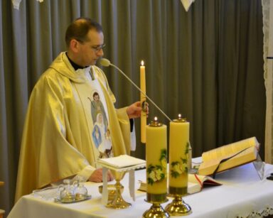 Sala. Ksiądz proboszcz Tomasz Kosewski stoi przy ołtarzu. Trzyma zapaloną gromnicę.
