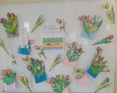 Zbliżenie. Tablica, na niej poprzypinane tulipany w kopertach, list oraz rozkład linii 144.