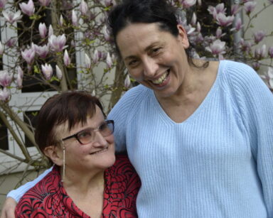 Ogród. Zbliżenie. Dwie uśmiechnięte kobiety pozują do zdjęcia. W tle drzewo magnolii.