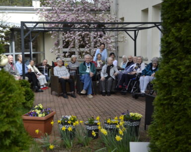 Ogród. Zbliżenie. Grupa osób pozuje do zdjęcia. W tle drzewo magnolii , żonkile, bratki.