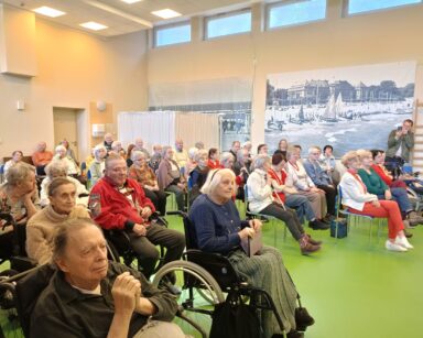 Sala. Na krzesłach siedzą seniorzy i patrzą na scenę.