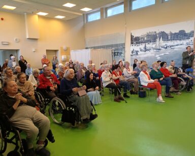 Sala. Seniorzy i opiekunowie DPS oglądają występy na scenie.