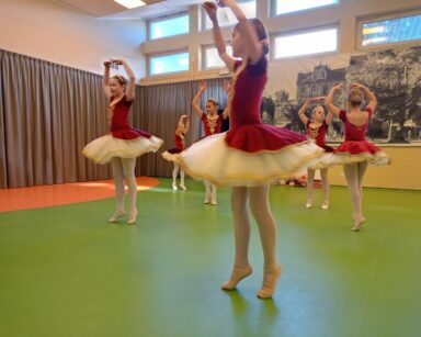 Scena. Na niej pięć małych baletnic czerwonych sukienkach i koronach na głowie. Baletnice kręcą piruety.