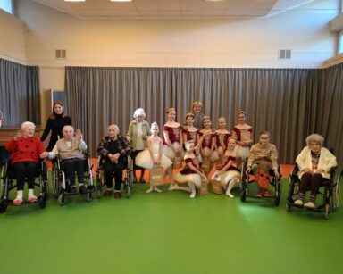 Sala. Młode baletnice pozują do grupowego zdjęcia z seniorami na wózkach i dwiema młodymi kobietami.