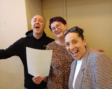 Zbliżenie. Dwie kobiety i mężczyzna pozują do zdjęcia. Wszyscy uśmiechają się, trzymają kartkę z piosenką.