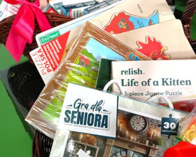 Zbliżenie. W koszu wiklinowym leżą różne gry planszowe oraz puzzle dla seniorów.