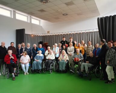 Sala. Grupa seniorów, opiekunów i koszykarze pozują do wspólnego zdjęcia.