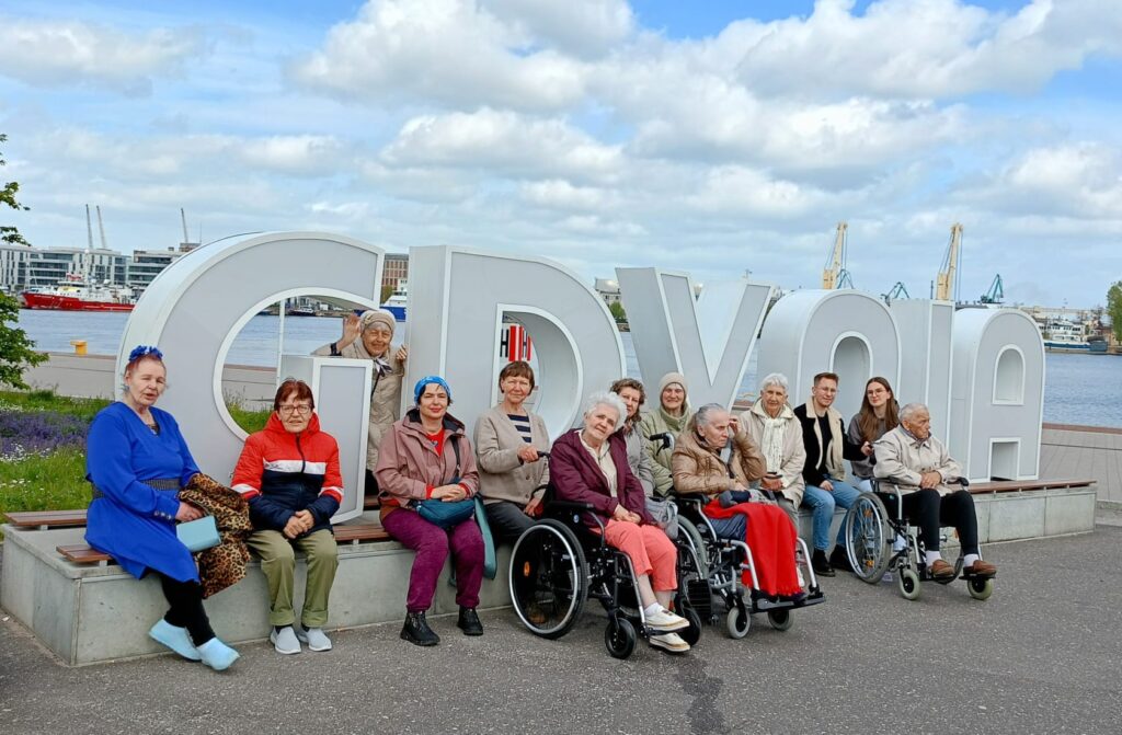 Molo południowe w Gdyni. Grupa seniorów i wolontariuszy pozuje do wspólnego zdjęcia przy napisie Gdynia.